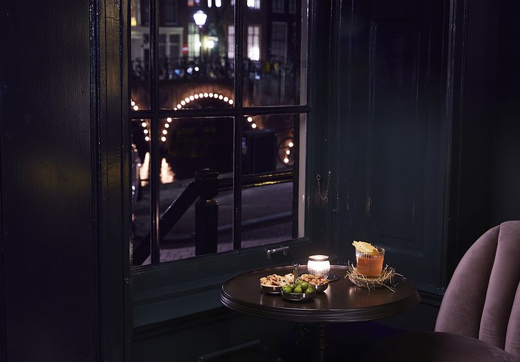 Pulitzer Amsterdam Pulitzer's Bar cozy window seat with drinks and snacks and view on the canal at night